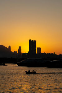 Silhouette buildings by sea against clear sky during sunset