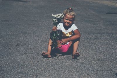 High angle view of girl golding flowers while sitting on road