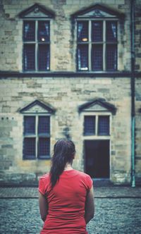 Rear view of woman standing by building in city