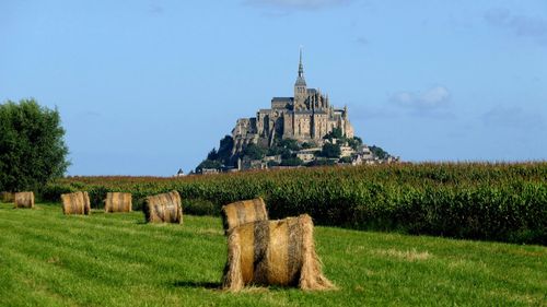 Hay bales on field by building against sky