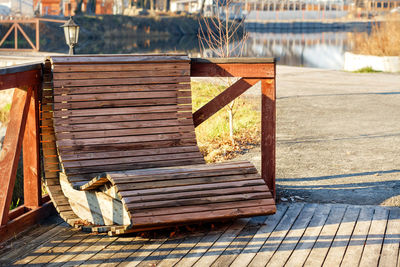 A wooden armchair with horizontal slats sits in a seating area by the river.