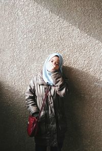 Portrait of young woman standing against wall