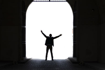 Silhouette man with arms outstretched standing below arch