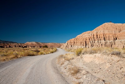 Road leading towards mountains against clear blue sky