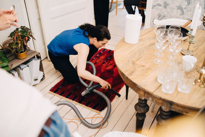 High angle view of mature woman cleaning hardwood floor with vacuum cleaner after party at home