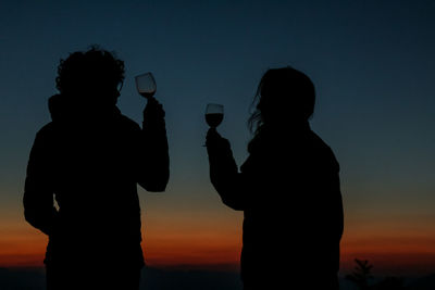 Silhouette man with arms raised against sky during sunset
