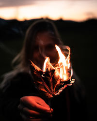 Close-up of woman holding burning leaf at sunset