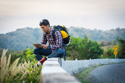 Full length of man sitting on mobile phone against sky