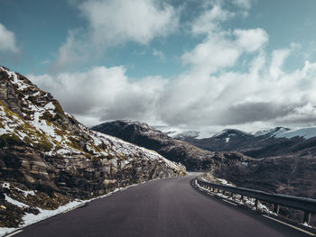 Empty road amidst snowcapped mountains against sky