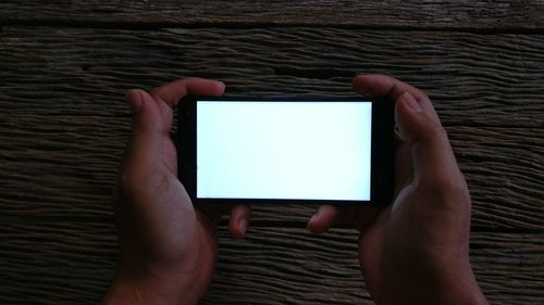 Cropped hands of person using mobile phone on wooden table