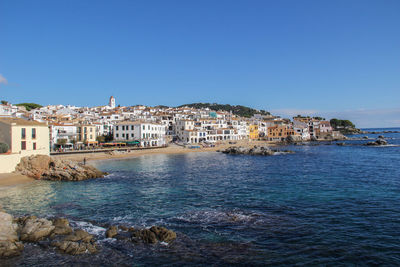 Buildings by sea against clear blue sky