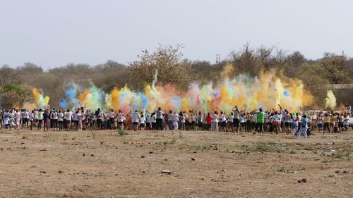 Group of people playing holi on field against clear sky