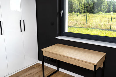 A wooden table under the window in a modern boy room in black and white colors, with vinyl panels. 
