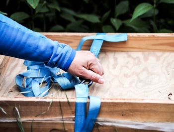 Cropped hand holding blue strap on wooden box
