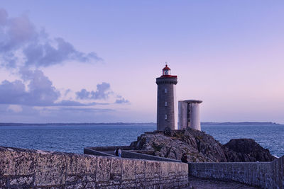 Lighthouse by sea against sky during sunset