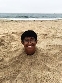 Portrait of smiling teenage boy in sand at beach