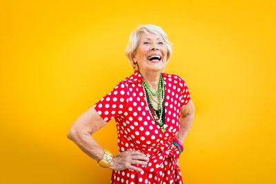 Smiling senior woman standing against yellow background