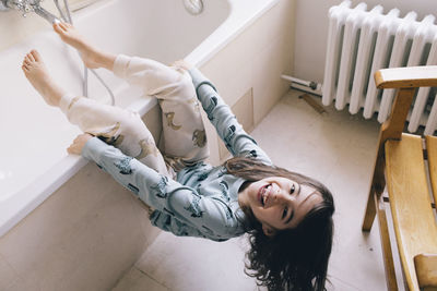 Portrait of playful girl hanging on bathtub