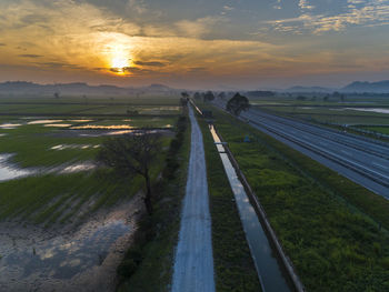 Panoramic view of road amidst field against sky during sunset