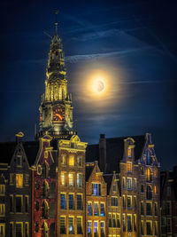 Old church tower of amsterdam with dutch houses and the moon during the bluehour in the netherlands.