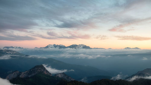 Glow on slope of mountain ridge lit by setting sun in scenic valley with cloud sky
