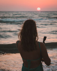 Rear view of woman looking at sea during sunset