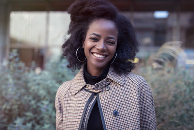 Beautiful african american woman with afro and large hoop earrings in stylish coat, street portrait