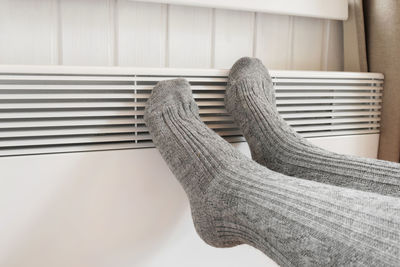 Legs in knitted socks warming over electric heater. frozen woman wearing a warm woolen socks