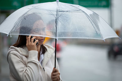 Woman talking on phone while standing with umbrella