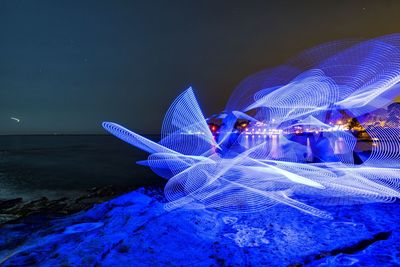 Light trails in sea against sky at night