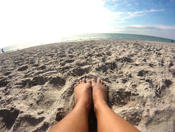 Low section of woman relaxing on beach against sky