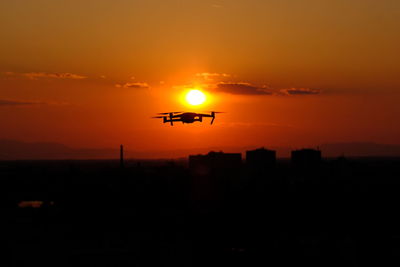 Silhouette airplane flying against orange sky