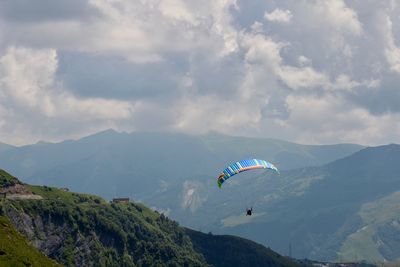 Person paragliding over mountain against sky