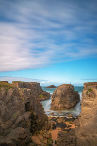 Rocks on shore by sea against sky