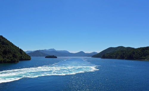 Scenic view of sea and mountains against clear blue sky