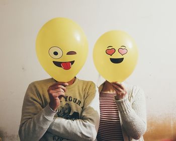 Man and woman with face covered by balloons against wall
