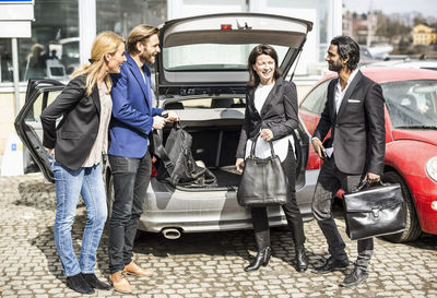 Business people communicating while unloading bags from car trunk