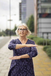 Portrait of woman gesturing while standing on footpath against buildings