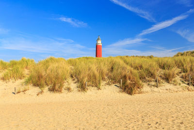 Lighthouse by beach against sky