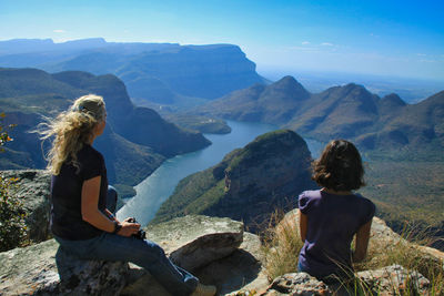 Rear view of mother with daughter sitting on rock against mountain and sky