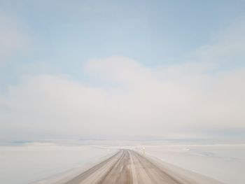 Empty road amidst snowy fields against sky
