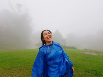 Portrait of smiling young woman standing on field during foggy weather