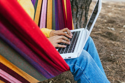 Cropped unrecognizable teen female chilling in hammock in park and browsing laptop