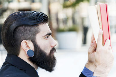 Young hipster reading a book sitting outdoors