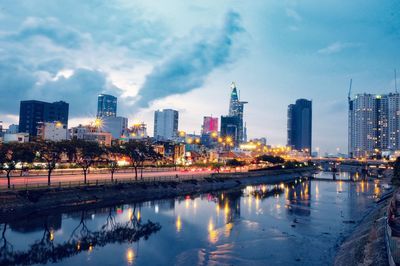 Reflection of illuminated buildings in river against sky