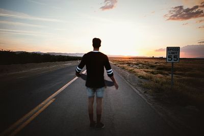 Rear view of man on road against sky during sunset