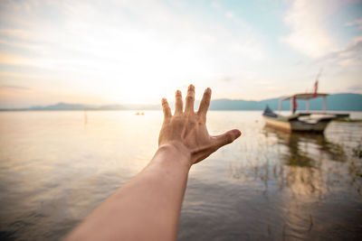 A hand reaching for the horizon with a beautiful lakeside landscape.