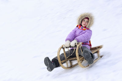 Portrait of girl playing on sled at snow covered field 