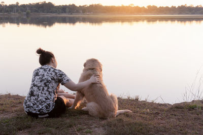 Rear view of woman with dog sitting by lake