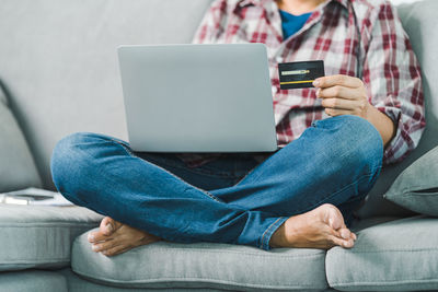 Midsection of man using mobile phone while sitting on sofa